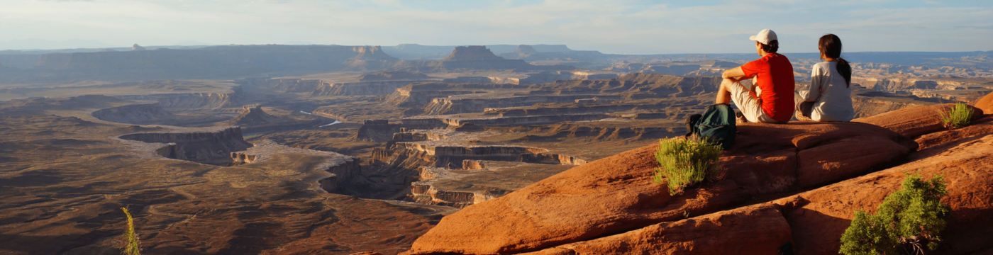 Two people sit next to each other, overlooking a red canyon