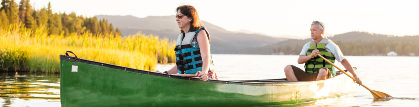 Adventurous woman and man in a canoe on the river with mountain in the background