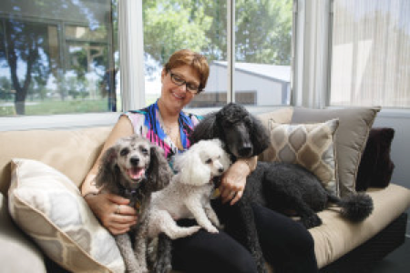 Mary F. posing on her couch with three small dogs on her lap