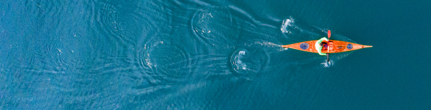 Top-down photograph of an individual in a bright orange kayak on a deep blue lake