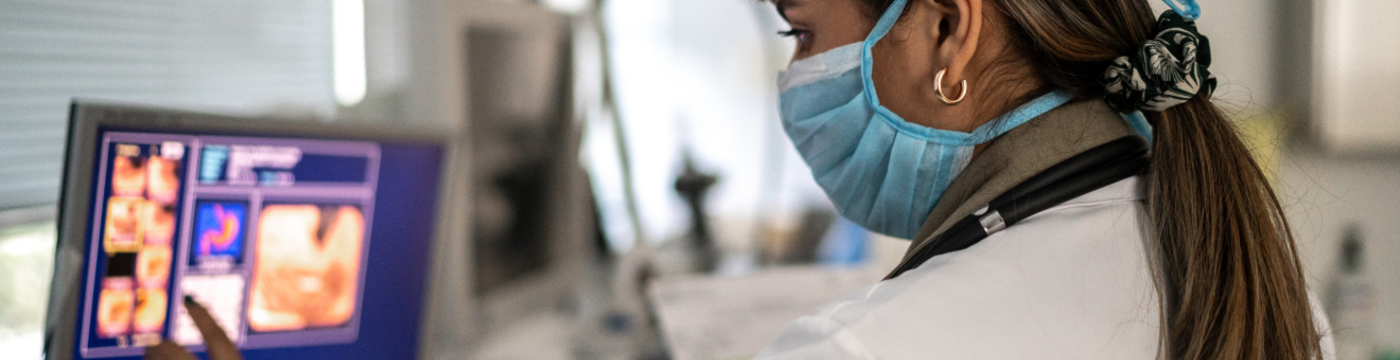 A clinician wearing a blue surgical mask analyzes medical scans on a screen