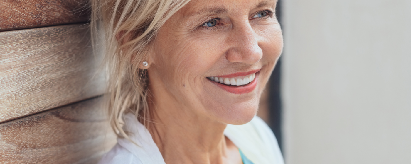 A smiling older woman leans against a wall