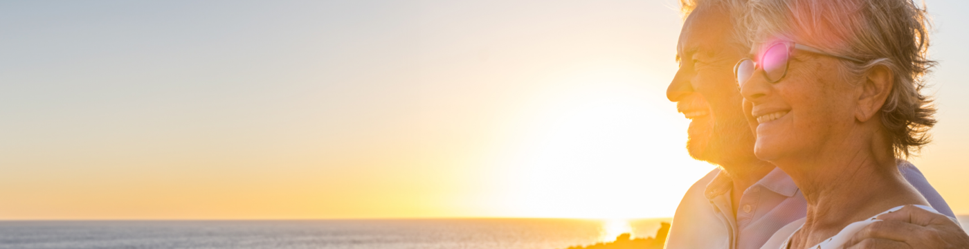 An older couple watch the sun set over the ocean