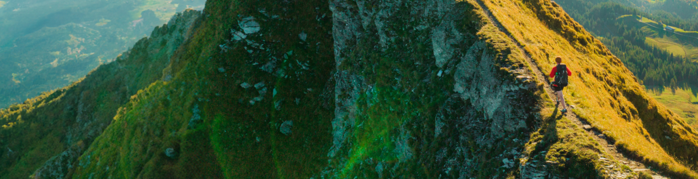 A woman ascends a steep path up the sun-lit side of a mountain